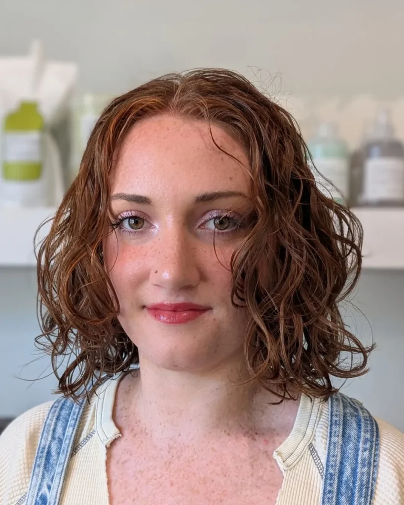 A woman with a curly wavy long bob in an auburn tone with a natural wet texture finish.