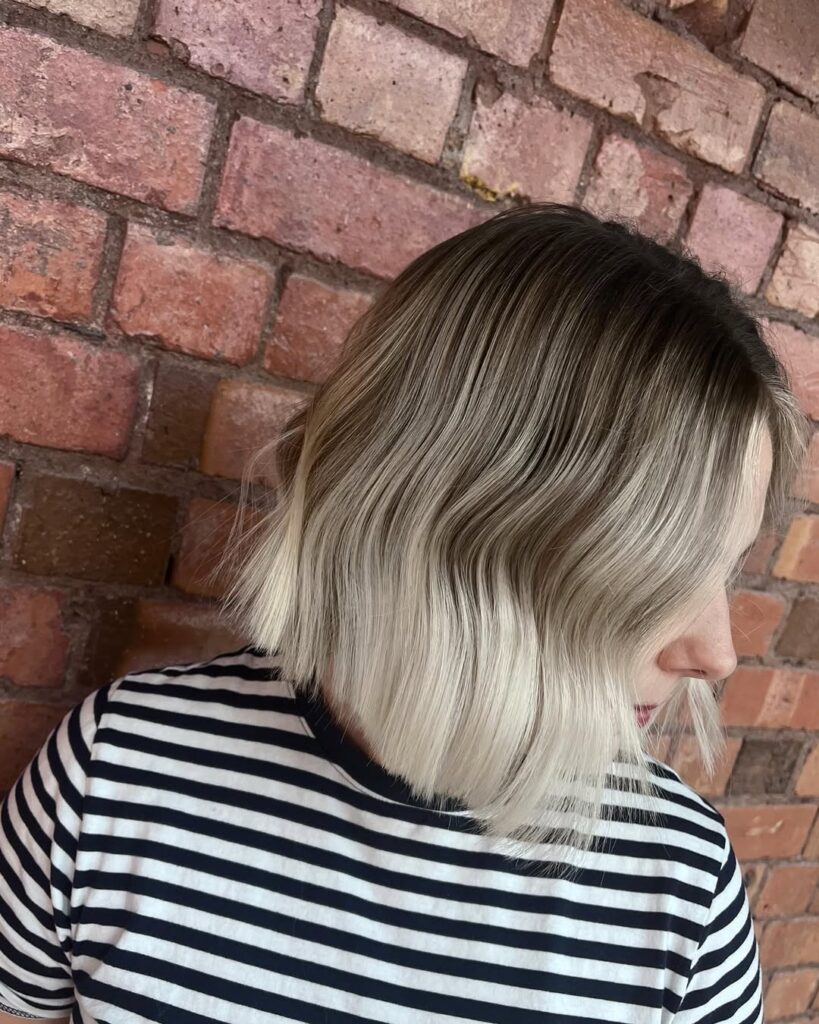 A woman with a wavy long bob featuring dark roots and light blonde ends with soft waves.