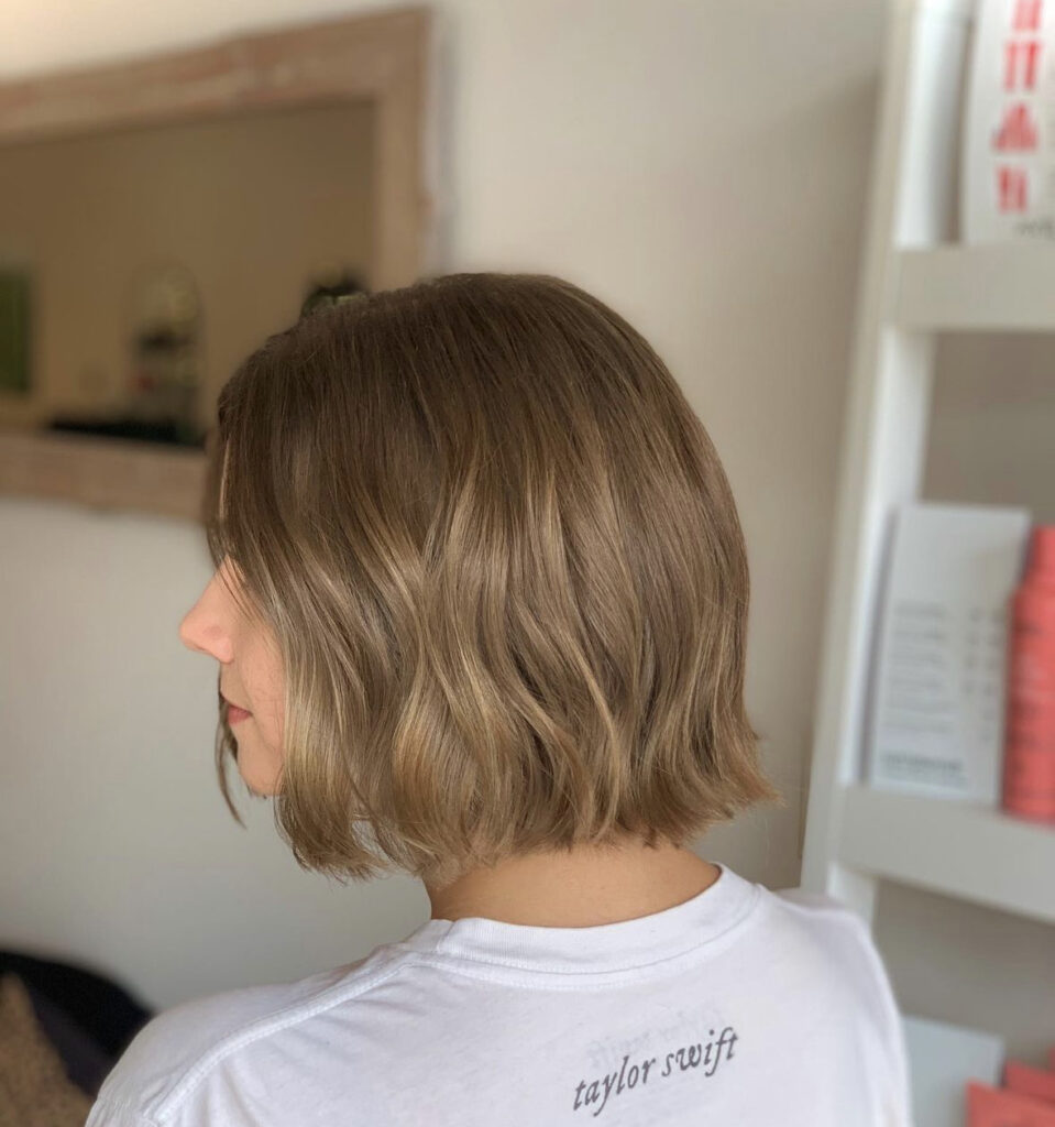 A woman with a sleek wavy long bob in a light brown tone with softly tapered ends.