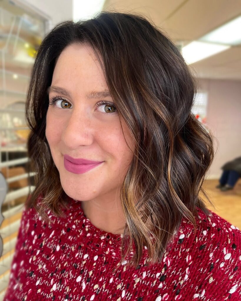 A woman with a brunette wavy long bob with soft face framing layers and loose waves.