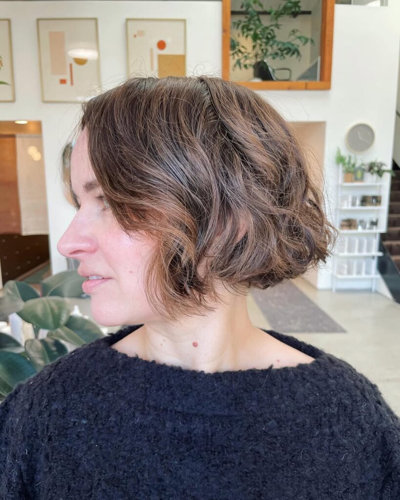 A woman with a soft wavy long bob in a warm brown shade with natural volume and light layers.