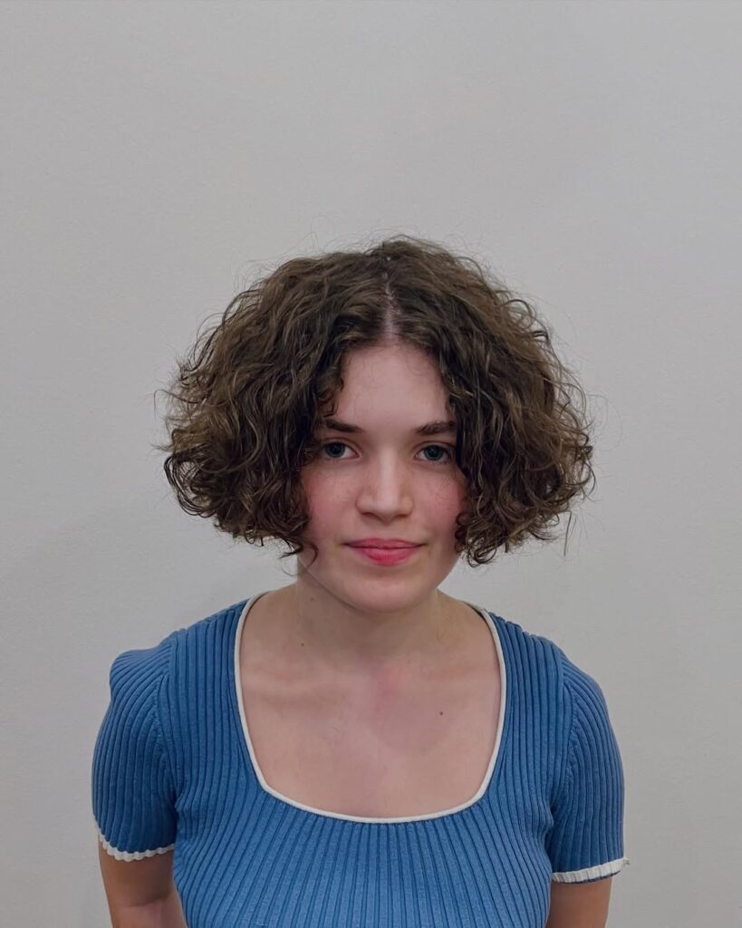 A woman with a rounded curly bob in a natural dark brown shade with soft volume.