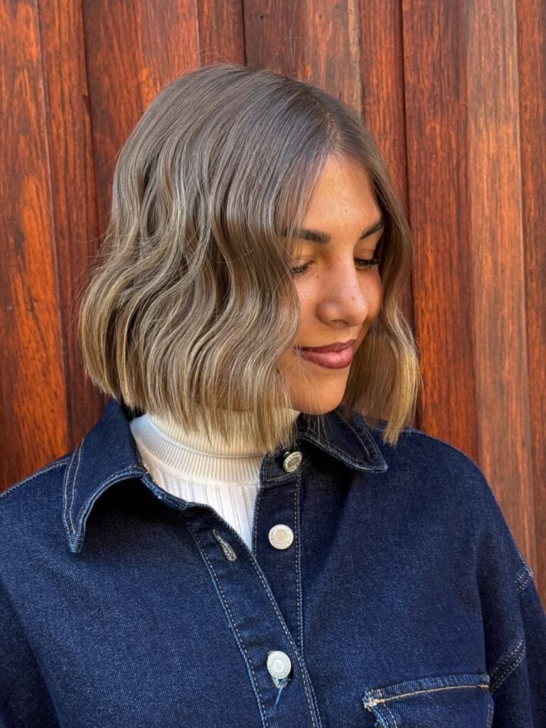 A woman with an ash brown wavy long bob with a soft blunt shape and loose waves.