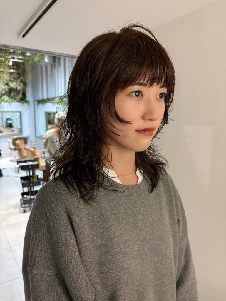 A woman with a dark brown choppy shag haircut featuring wispy bangs and piecey layers that curve toward the face.