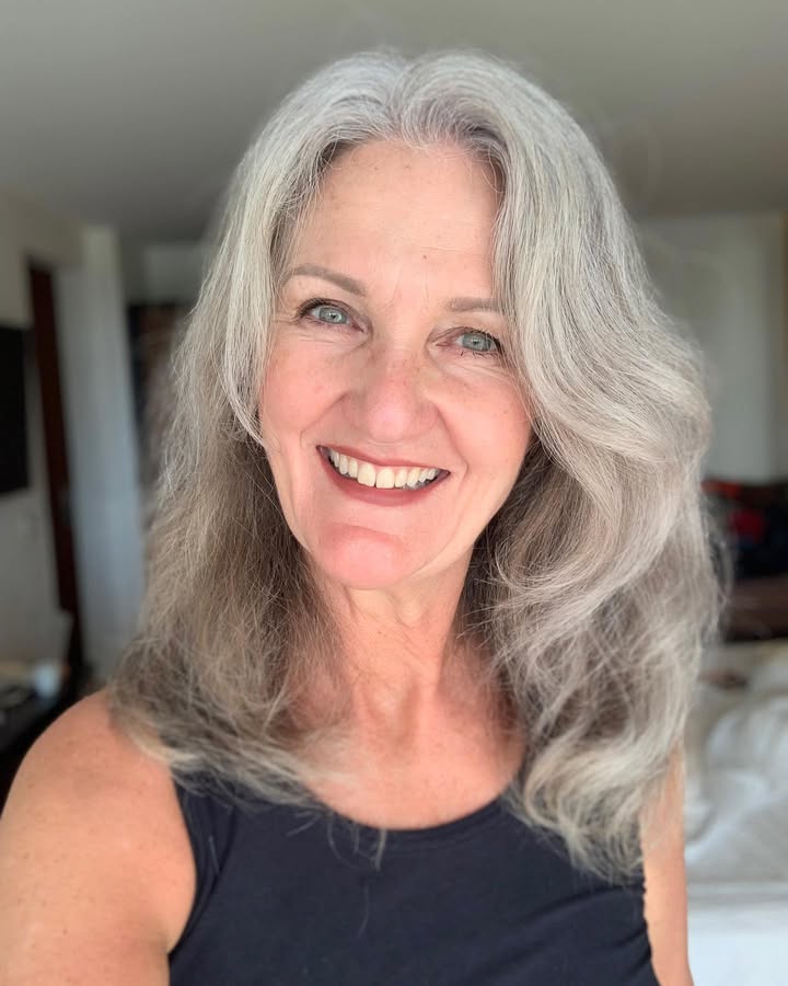Long silver wavy hair with wispy bangs softly framing the face.