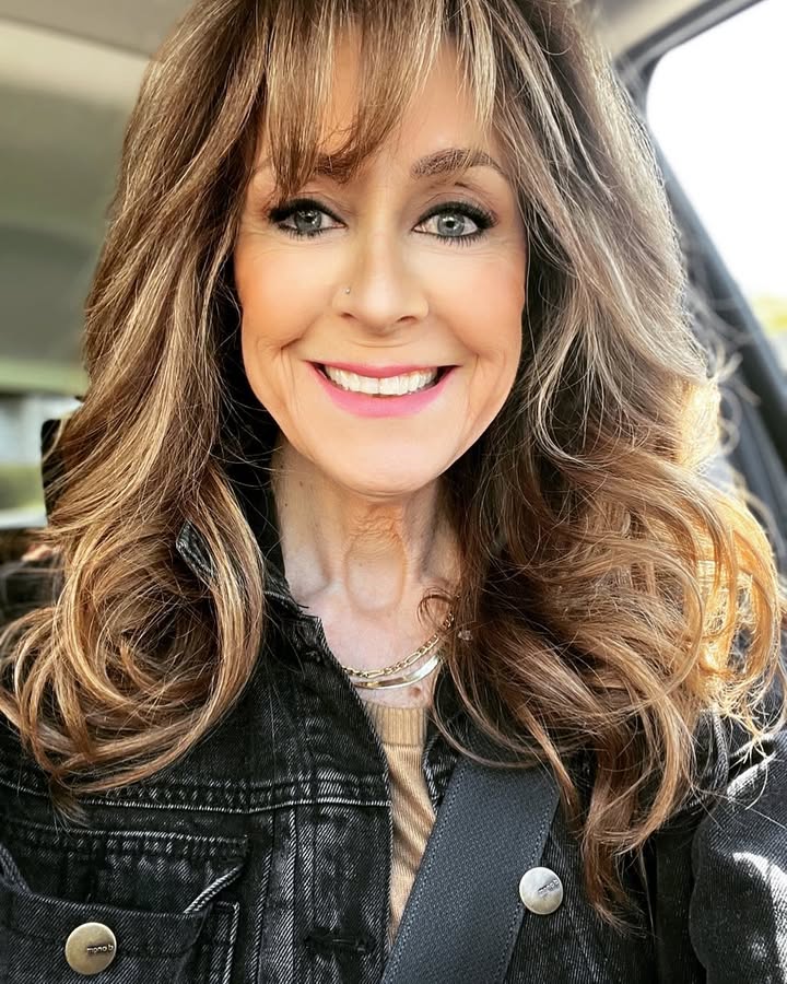 Long layered brown hair with rounded bangs and soft voluminous curls.