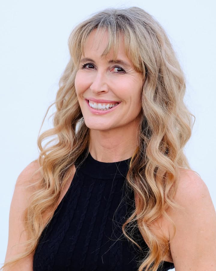 Long blonde layered hair with feathered bangs and soft volume.