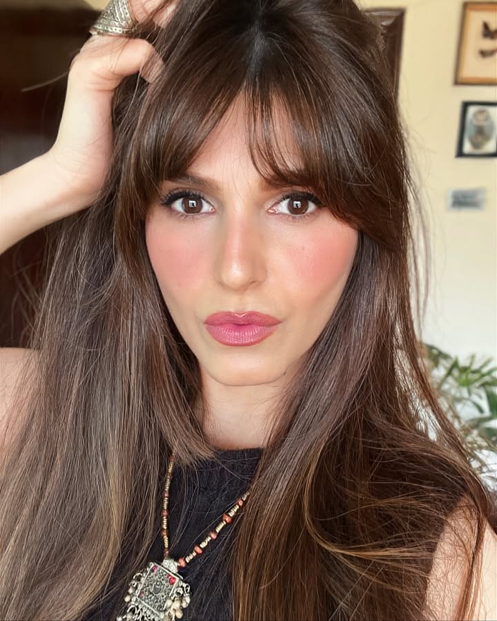 Long brunette layered hair with full fringe and soft volume.