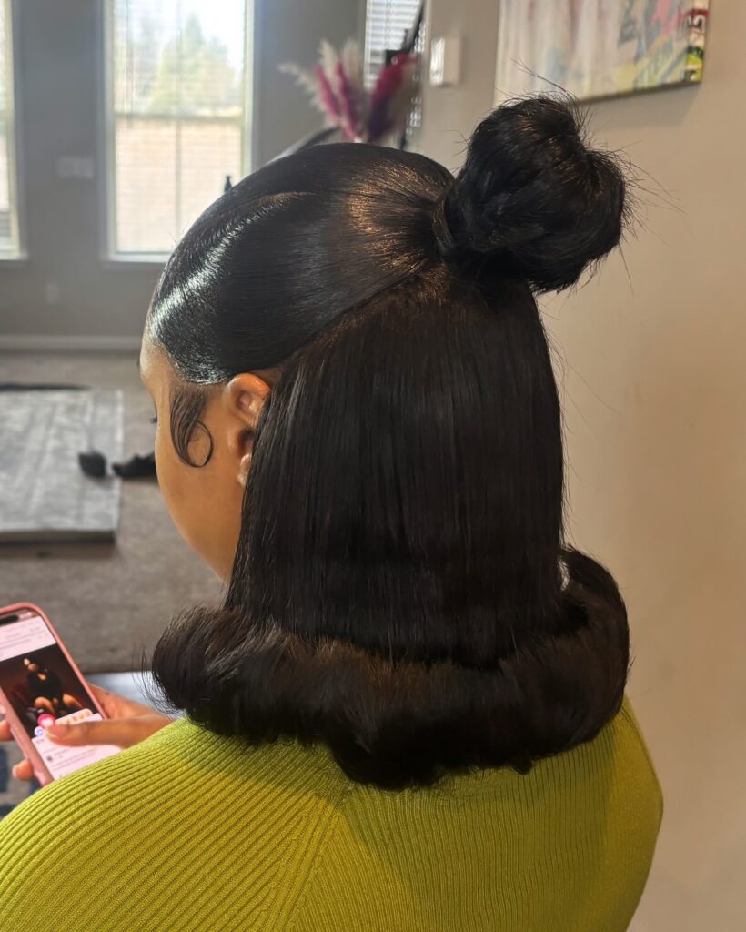A woman with sleek black hair in a half-up bun with dramatic upward-flipped ends and styled edges.