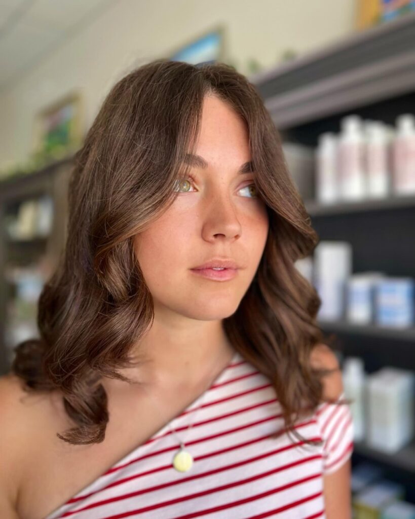 A woman with medium-length chestnut-brown hair styled in soft waves with outward-flipped face-framing layers.