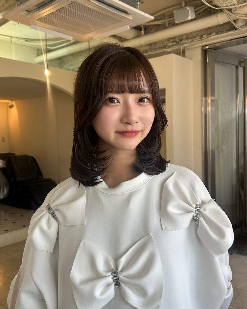 A woman with medium-length dark brown hair featuring wispy bangs and soft face-framing layers curved inward.