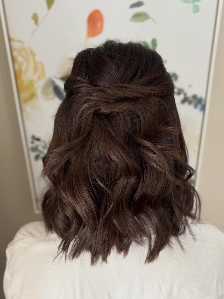 A rear view of a woman with medium-length dark brown hair styled in a braided half-up look with textured waves.