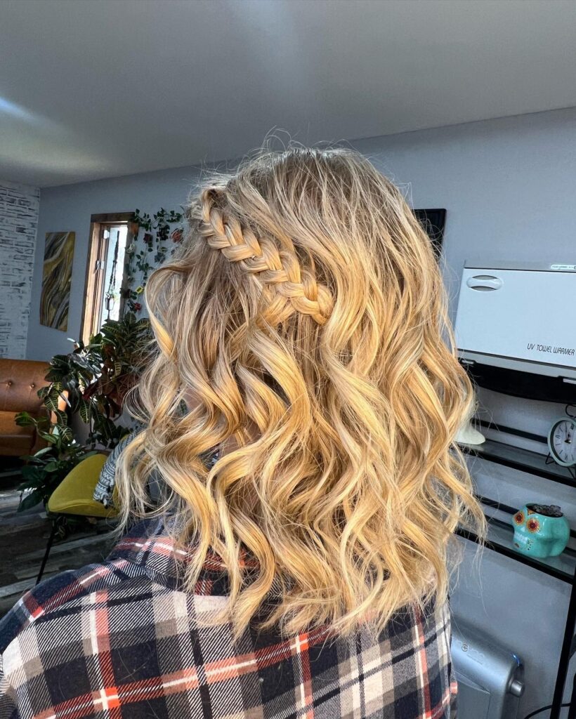 A woman with medium-length bright blonde curly hair is seen from behind with a thick Dutch braid tucked into the side.