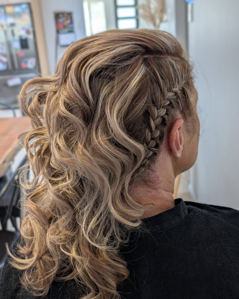 A woman viewed from the side with her sandy blonde hair styled into a textured faux hawk featuring a tight side braid and voluminous curls.