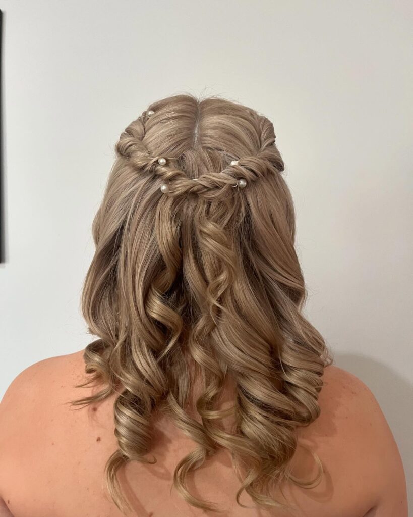 A woman viewed from the back with sandy blonde hair styled in a half-updo with two side twists meeting in the middle and accented with small white pearls.