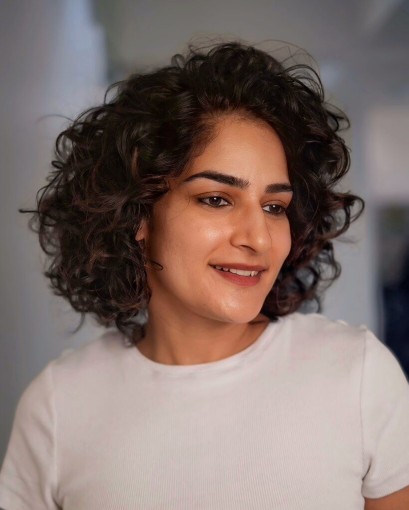 A woman with a neck-length dark brunette curly shag hairstyle featuring lots of volume and layered ringlets.