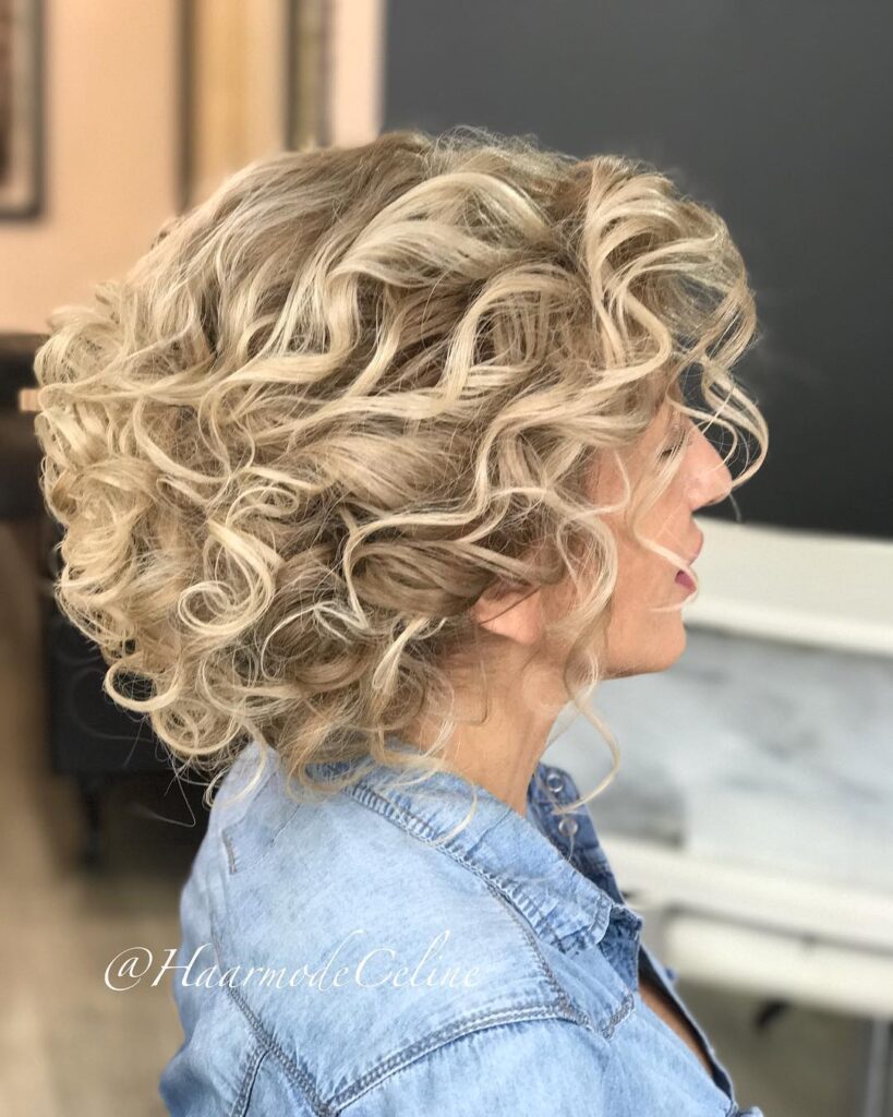 A woman with a tapered neck-length ash blonde hairstyle featuring voluminous bouncy curls and platinum highlights.