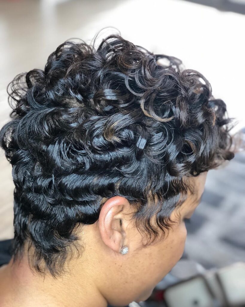 A woman with a short dark brunette pixie cut featuring tight curls on top and sculpted finger waves along the sides.