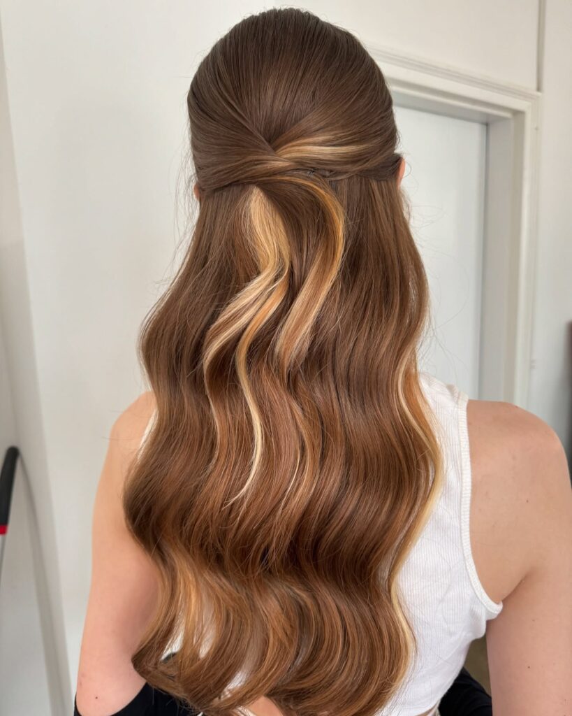 A woman with long brown hair and bold blonde highlights in a simple half-updo twist with soft waves.