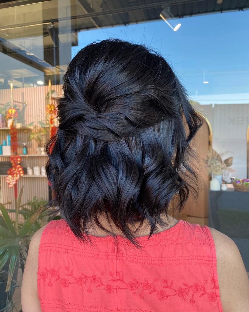 A woman with a black, wavy, long bob styled in a loose braided half-updo.