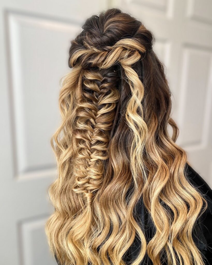 A woman with long, wavy blonde ombre hair featuring a wide, textured fishtail braid in a half-updo.