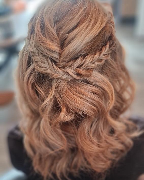 A woman with medium-length strawberry blonde hair in a half-updo featuring two fishtail braids pinned into a crown at the back.