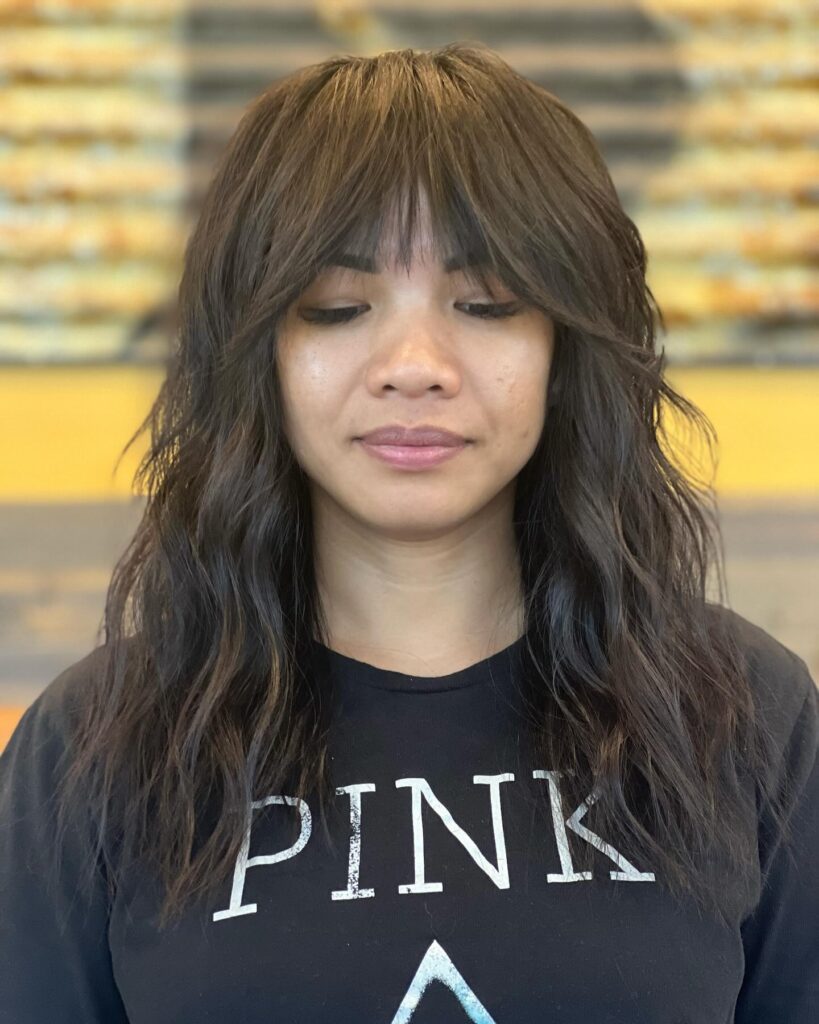 A woman with a dark brunette medium-length shag haircut featuring curtain bangs and tousled waves.