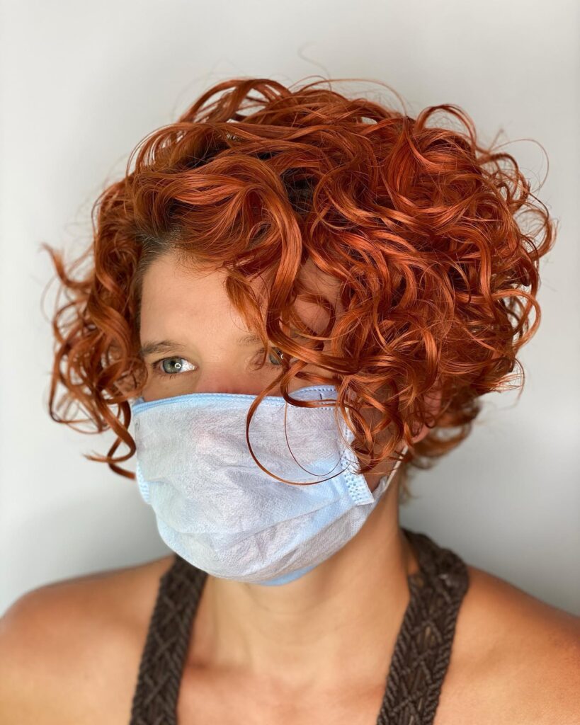 A woman with a chin-length curly bob in a bright and glossy copper-red color.