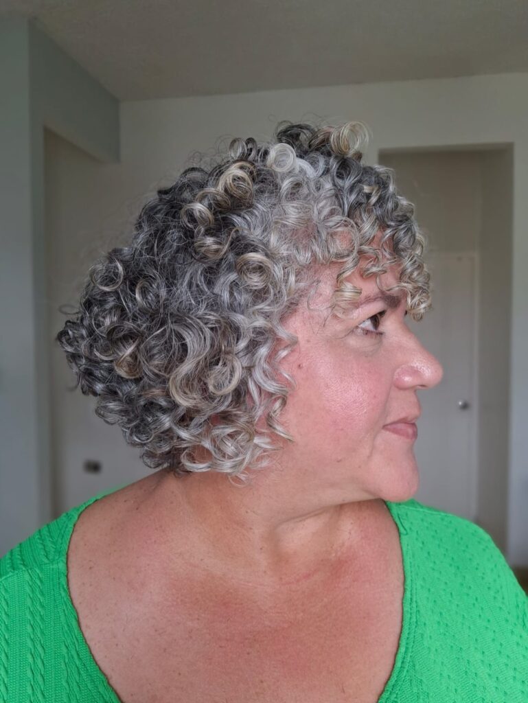 A woman in a green top is shown from the side with a short, angled bob made of natural silver and gray curls.