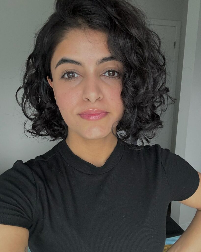 A woman with dark brown curly hair styled in a side-parted chin-length bob.