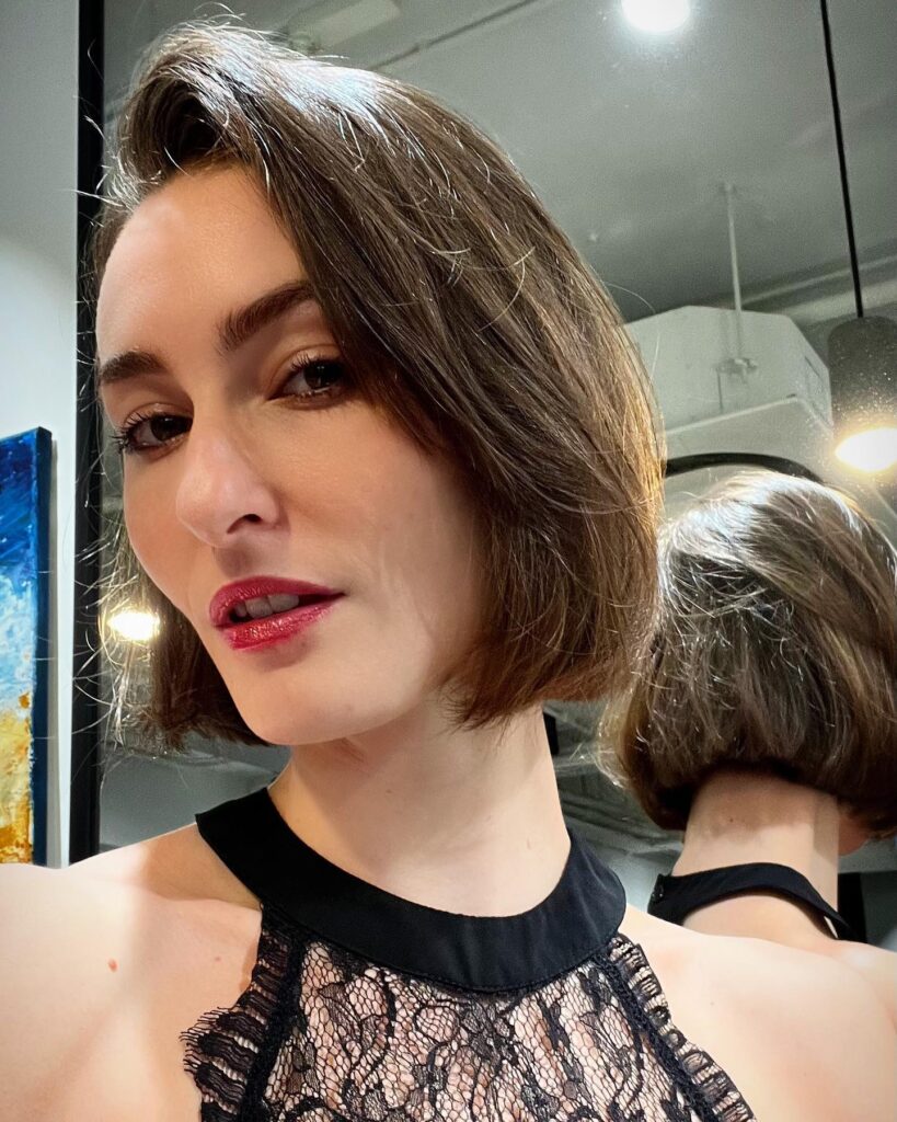 A woman with a chin-length chocolate brown French bob featuring a deep side part and smooth texture.