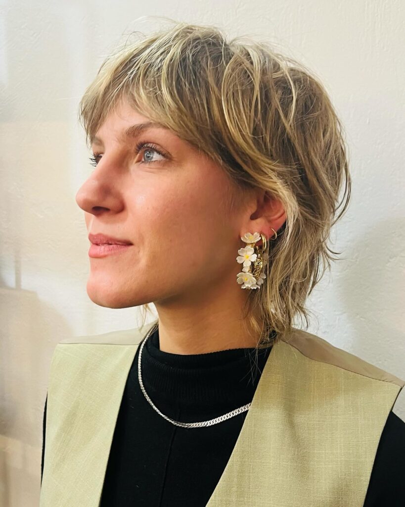 A woman with a short sandy blonde wolf cut featuring choppy layers and a tousled fringe.