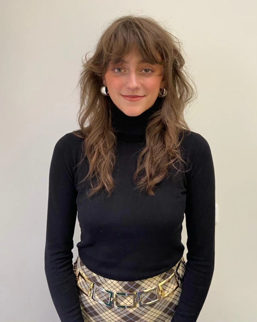 A woman with long mousy brown hair styled in a shaggy butterfly cut with voluminous layers and a piecey fringe.