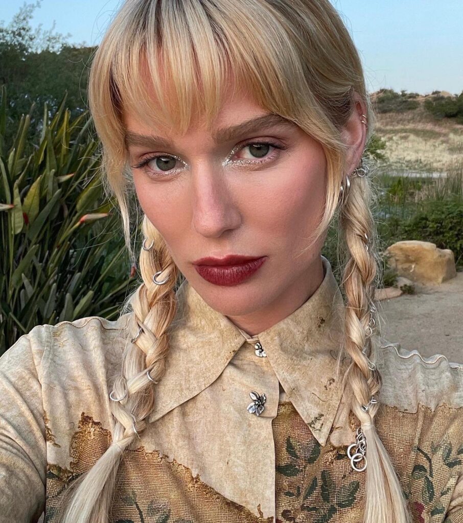 A woman with blonde hair styled in two long braids decorated with several small silver rings throughout the plaits.