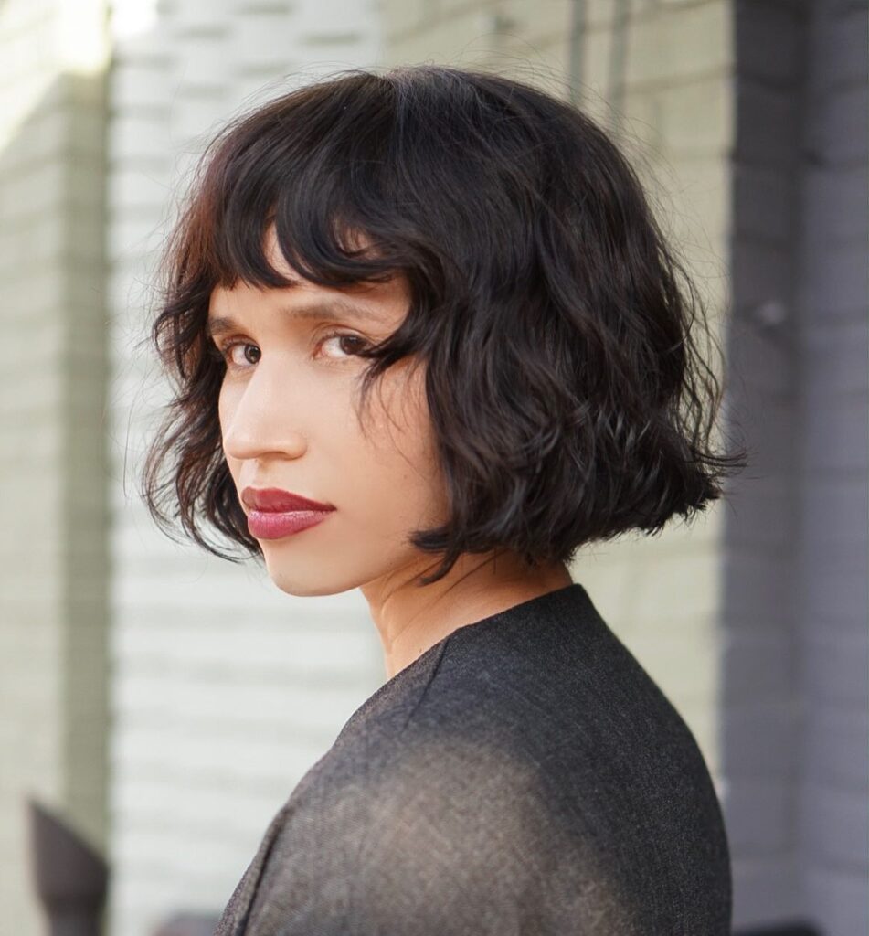 A woman with a chin-length dark brunette bob featuring soft wavy texture and a short piecey fringe.