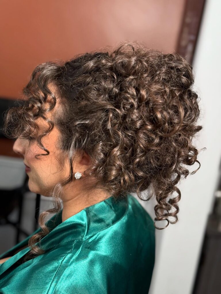 A voluminous curly bun with defined ringlets and loose tendrils framing the face.