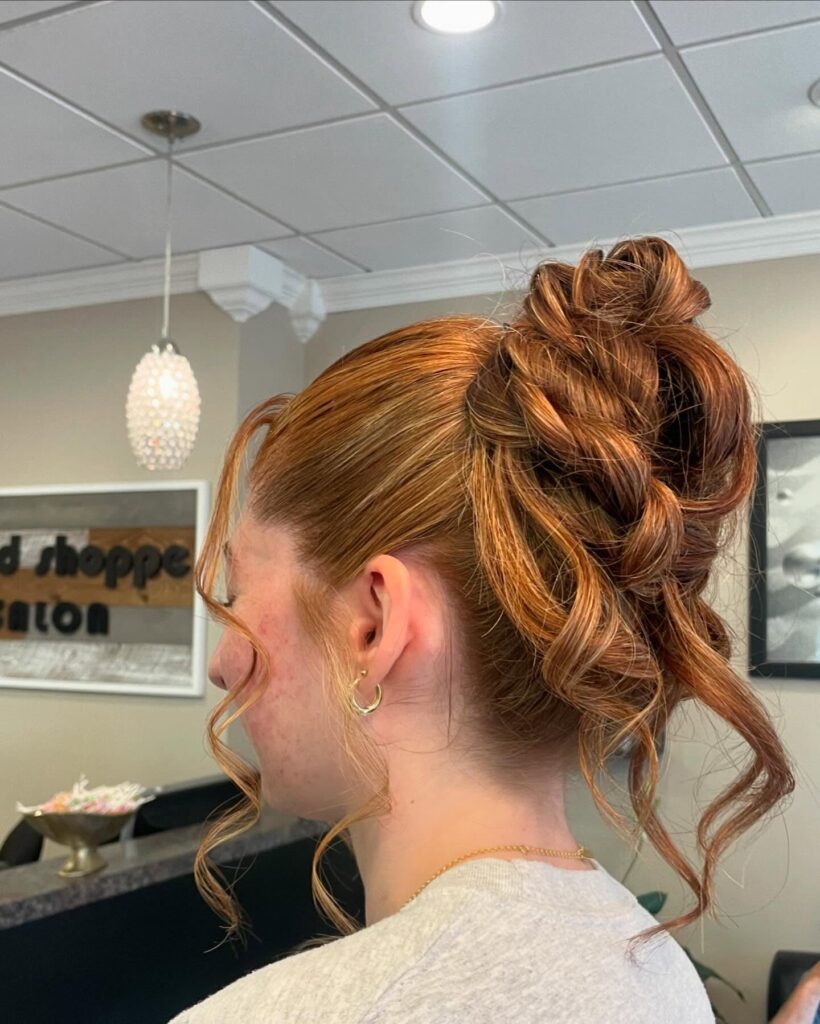 A high curly bun with copper tones and loose ringlets framing the face and neck.