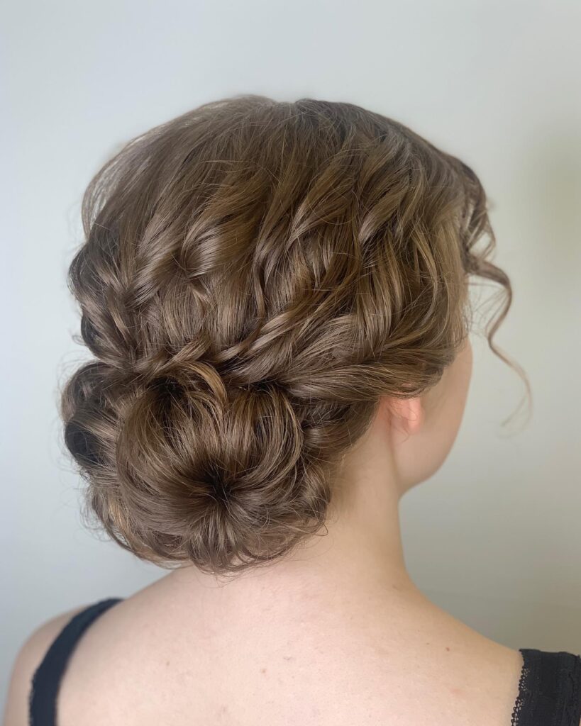 A soft twisted low curly bun with smooth brown hair and subtle loose strands around the face.