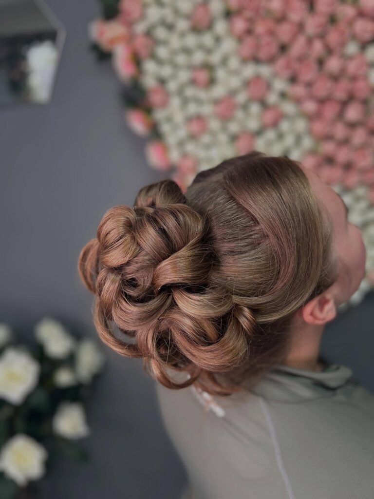 A polished curly bun with smooth roots and a rounded voluminous shape.