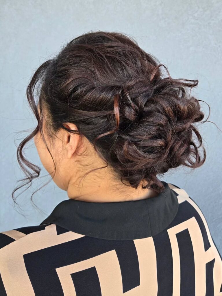 A dark braided low curly bun with soft texture and loose curls framing the face.