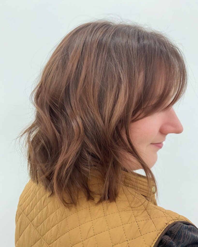 A light brown wavy bob with soft layers and wispy bangs creating a relaxed face framing look.