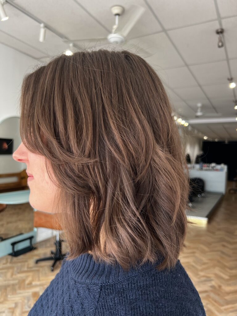 A mid length textured bob with soft layers and light bangs in a natural brown shade.