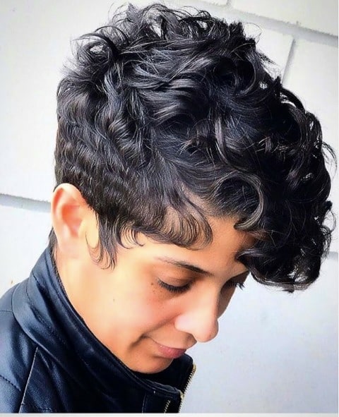 A woman with a short tomboy haircut featuring natural dark curls on top and closely cropped sides.