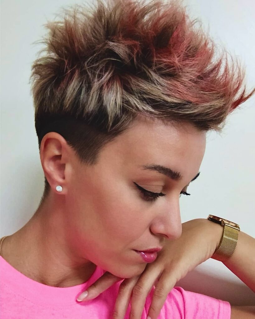 A woman with a spiky textured tomboy pixie haircut featuring short sides and a layered top with brown and reddish tones.