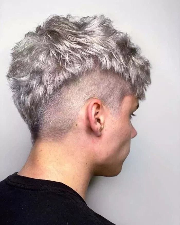 A woman with a silver textured tomboy haircut featuring shaved sides and a voluminous layered top.