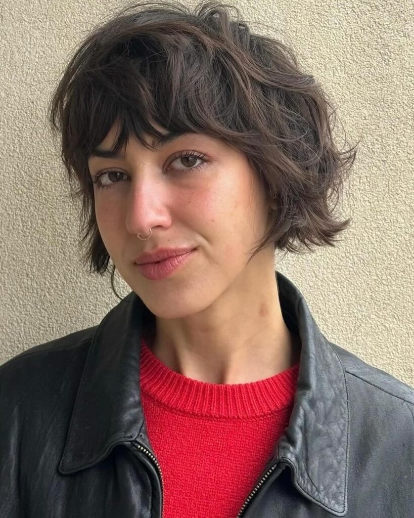 Short brunette French bob with soft waves and feathered bangs.