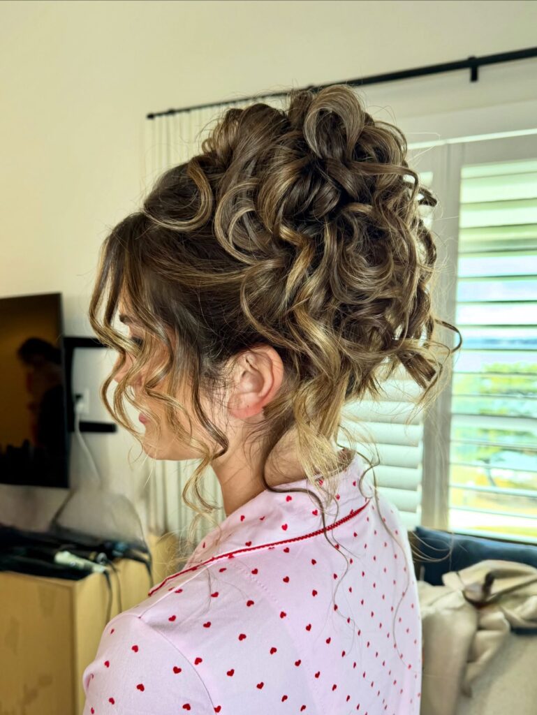 A voluminous curly updo with blonde highlights and loose curls framing the face.
