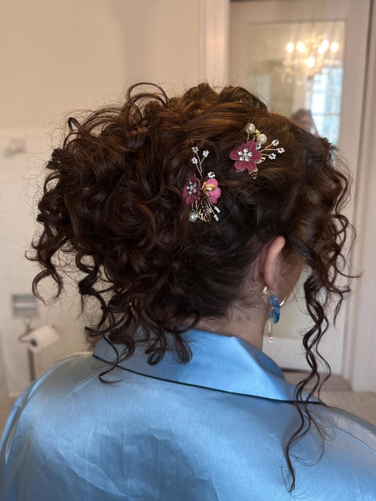 A curly updo with a textured bun and floral hair accessories with loose tendrils around the face.