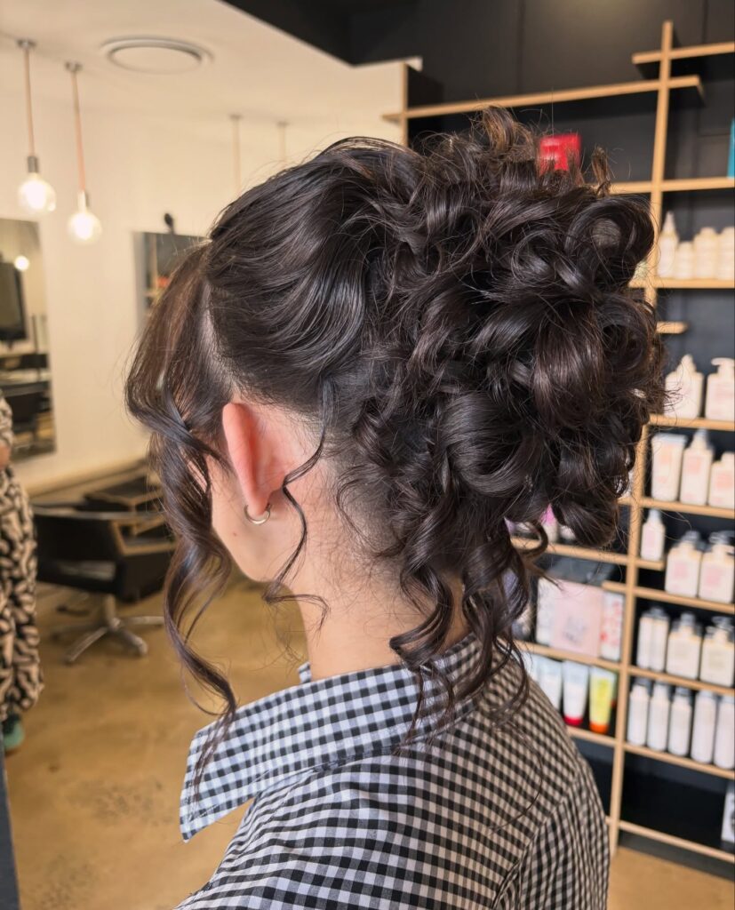 A textured curly updo with volume at the crown and loose curls framing the face.