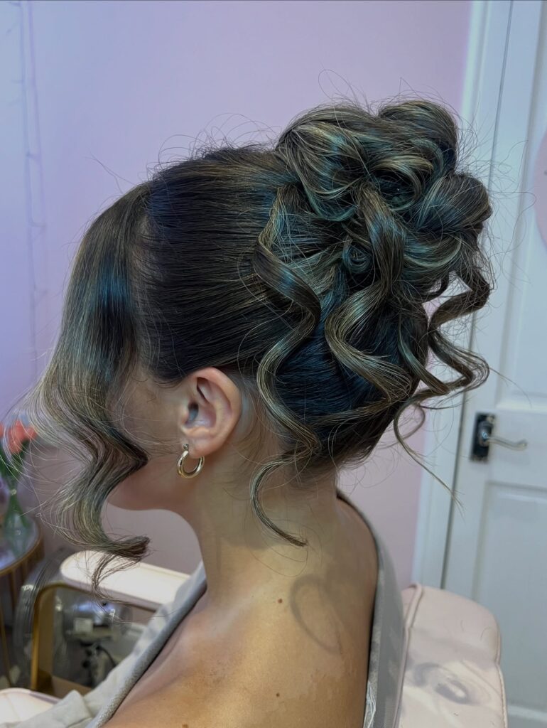 A sculpted curly bun with defined looped curls and soft face framing pieces.